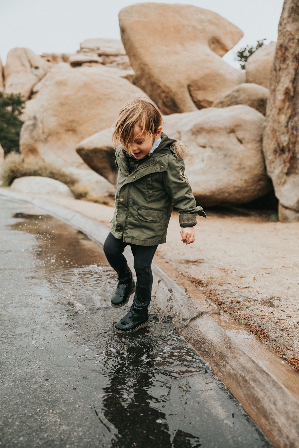 girl in green jacket and black pants walking on wet road during daytime