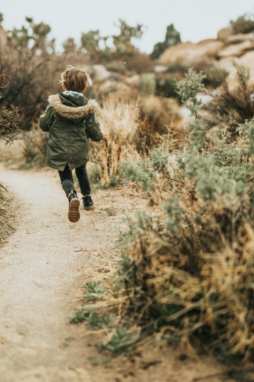 child in green jacket walking on dirt road during daytime