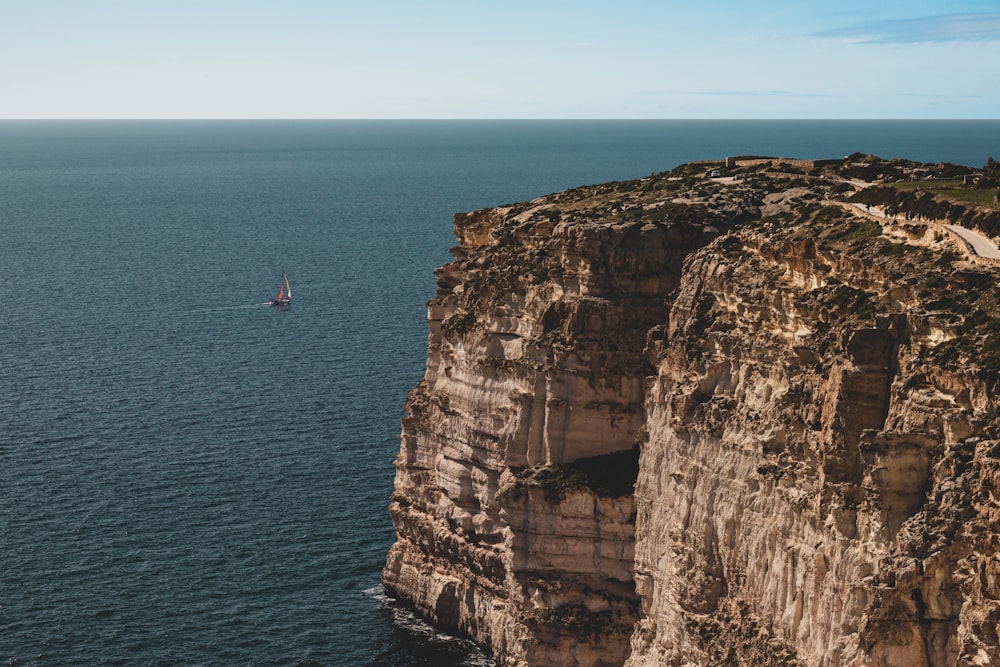 person in red shirt standing on cliff near body of water during daytime