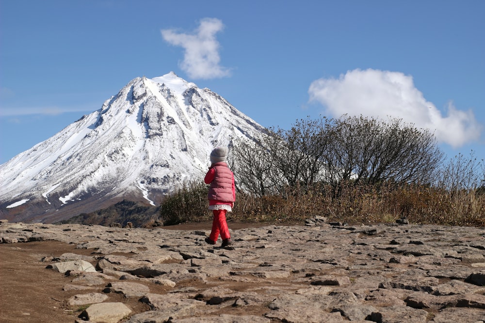 person in red jacket and red pants standing on brown field near snow covered mountain during
