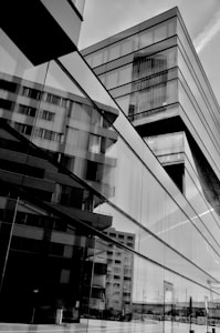 Modern architecture with glass panels reflecting surrounding buildings, creating a complex interplay of shapes and angles. The clean lines and reflective surfaces convey a sense of sophistication.