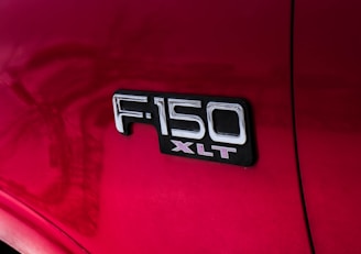 A close-up view of a red vehicle's side panel with the badge 'F-150 XLT' prominently displayed in chrome letters against a black background.