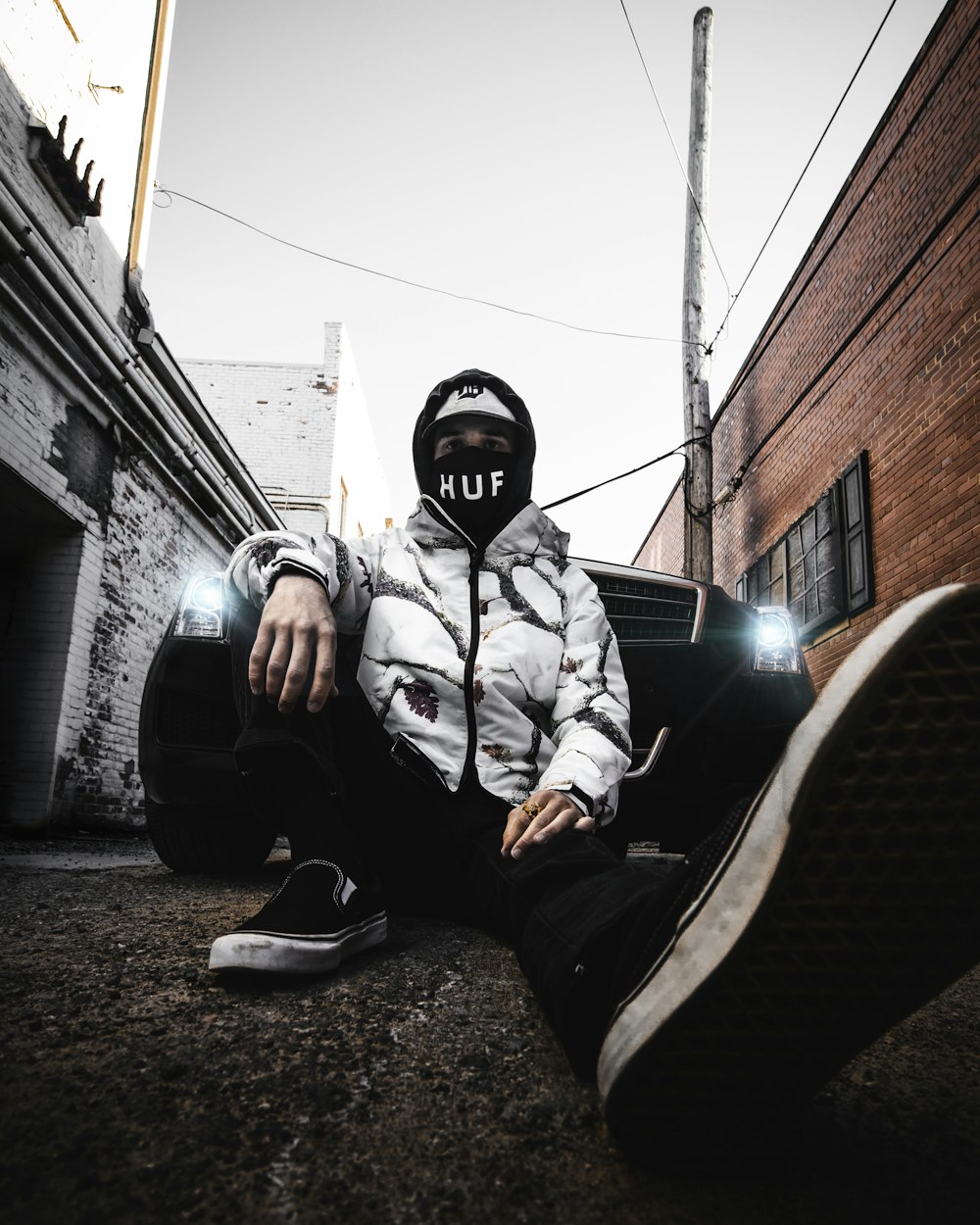 man in black and white jacket and black pants sitting on black car