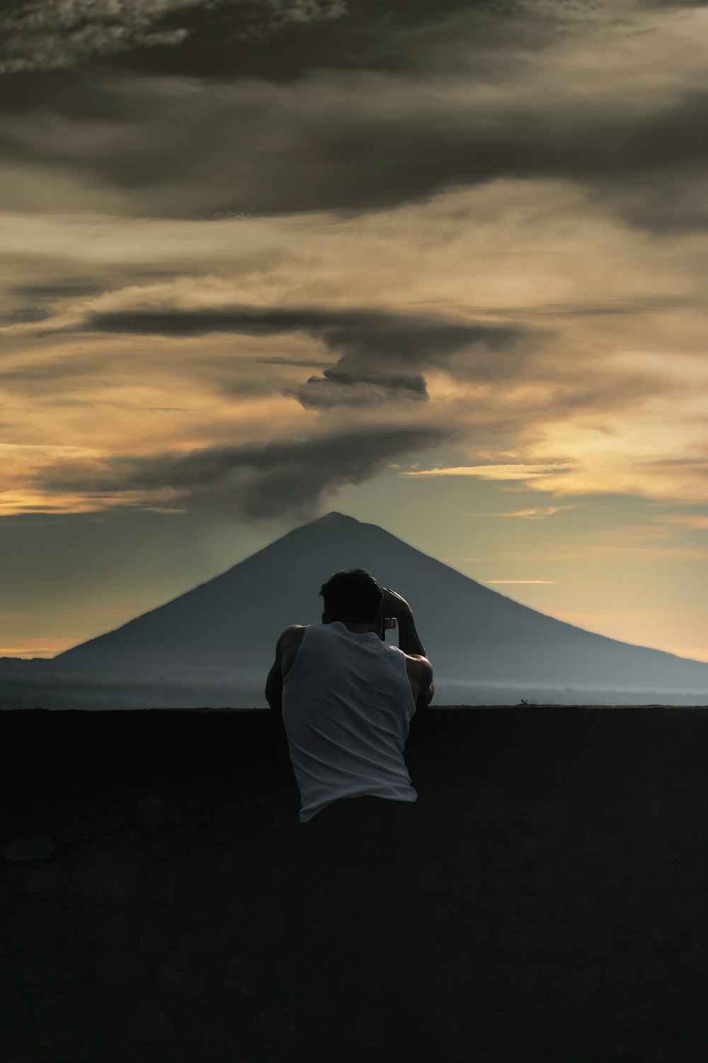 person in white shirt sitting on rock during sunset