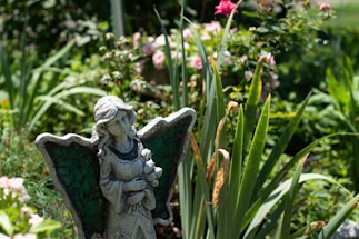 gray concrete angel statue near pink flowers during daytime