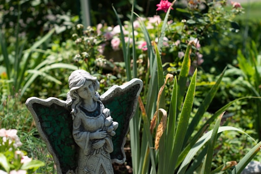 gray concrete angel statue near pink flowers during daytime