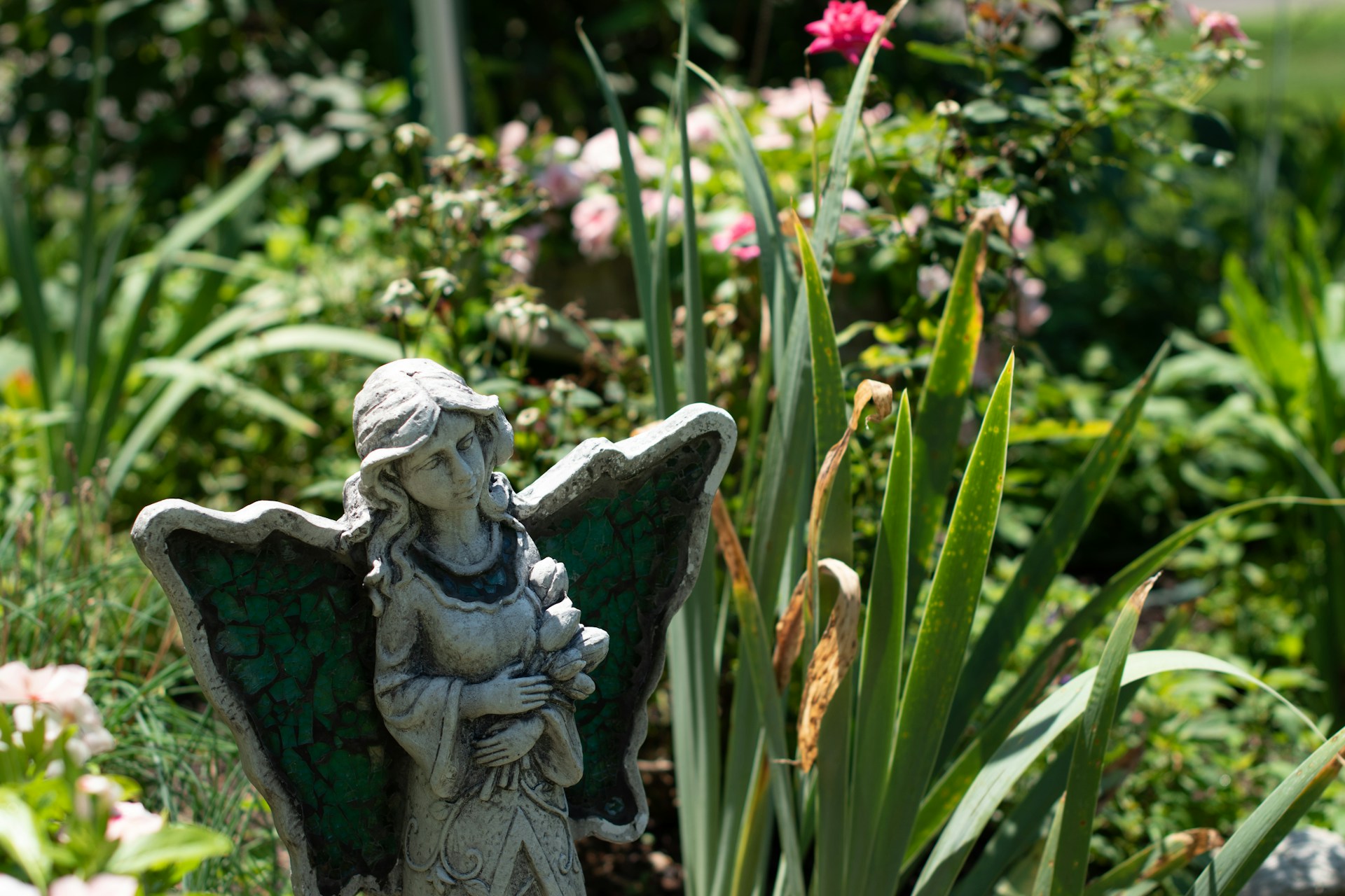 gray concrete angel statue near pink flowers during daytime