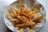 A plate of crispy golden french fries topped with melted cheese and garnished with herbs. The fries are served in a white bowl lined with branded paper.