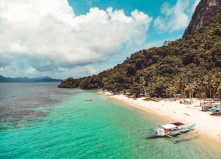 white boat on sea near brown and green mountain under white clouds and blue sky during