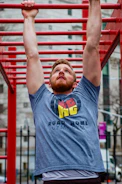 Male calisthenics athlete performing a muscle-up on outdoor bars, wearing a fitted compression shirt.