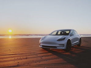 A compact car parked near a beach at sunset.