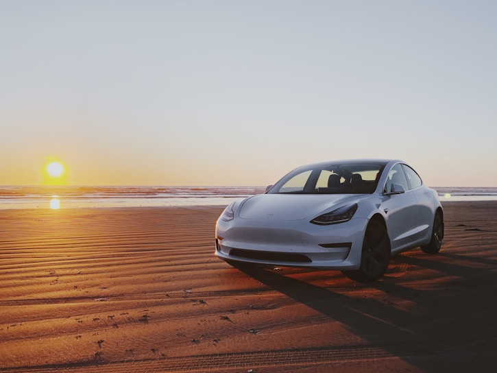 A sleek white convertible parked on a sunlit beach road with turquoise ocean waves in the background.
