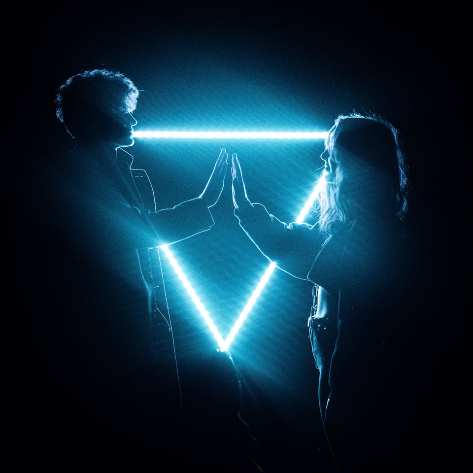 Two people in front of a neon triangle. The people aren't touching; they are disconnected.