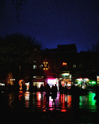 A dynamic urban night scene with glowing city lights and a silhouette of a person walking on asphalt.