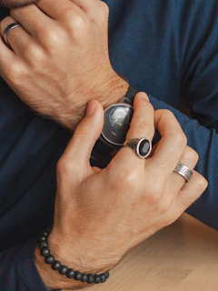 Lifestyle shot of a model adjusting a sleek watch and stacking rings in a cozy café setting