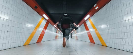 man in black jacket and black pants wearing black backpack walking on brown wooden floor in Caen France