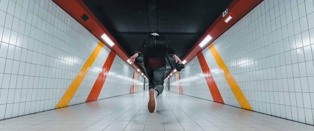 man in black jacket and black pants wearing black backpack walking on brown wooden floor