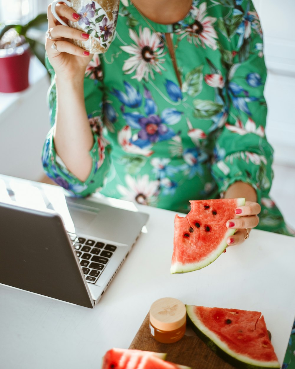 woman in green and white floral shirt holding sliced watermelon