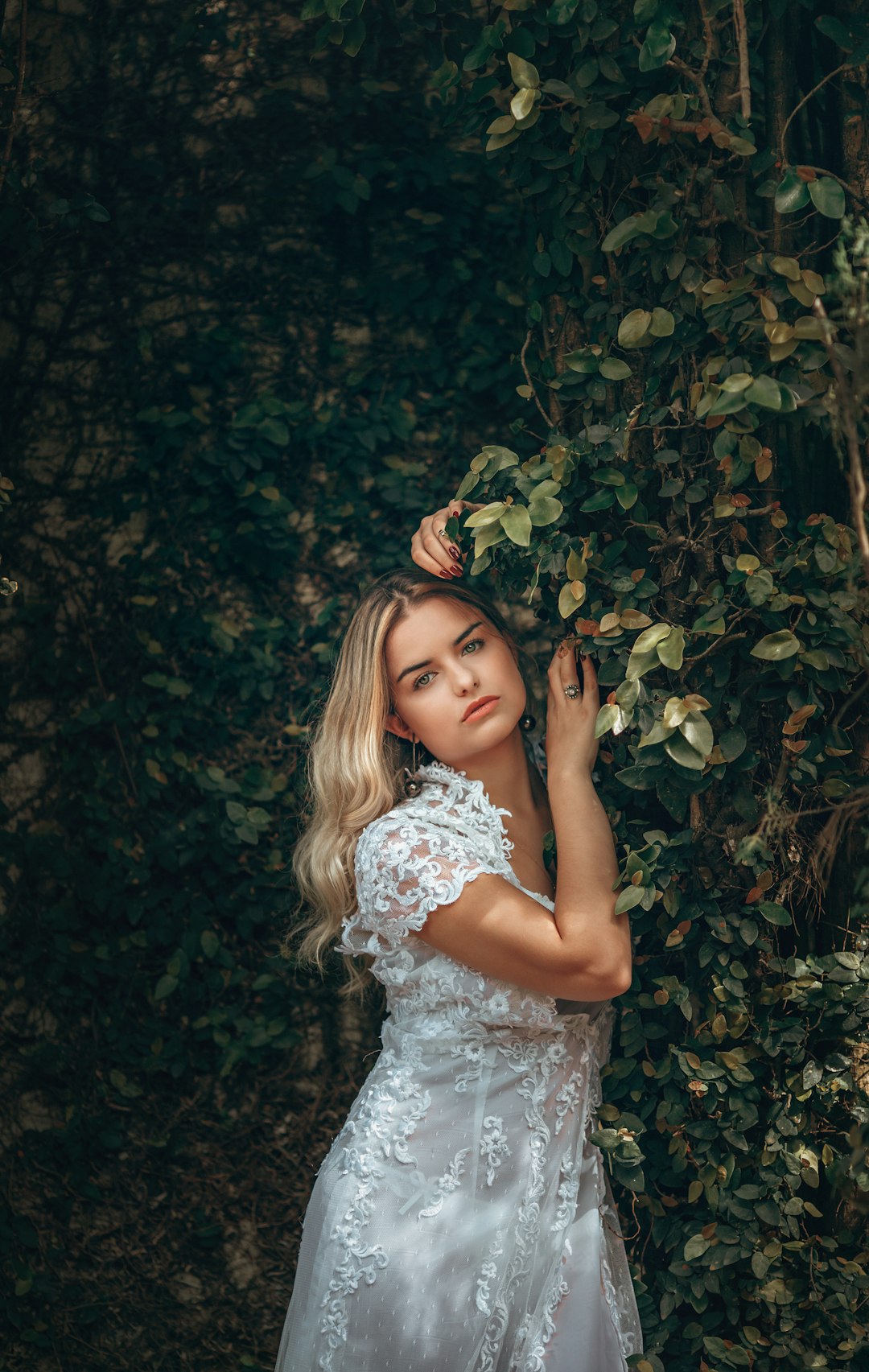 girl in white floral dress standing beside green plant