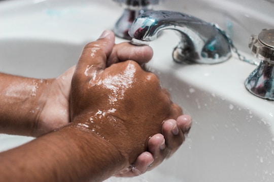 A pair of hands washing dishes with sudsy dish soap in a bright kitchen.