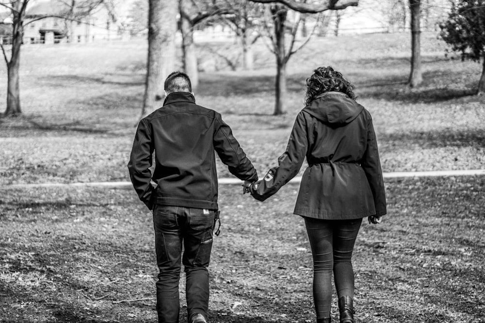 man and woman walking on grass field in grayscale photography