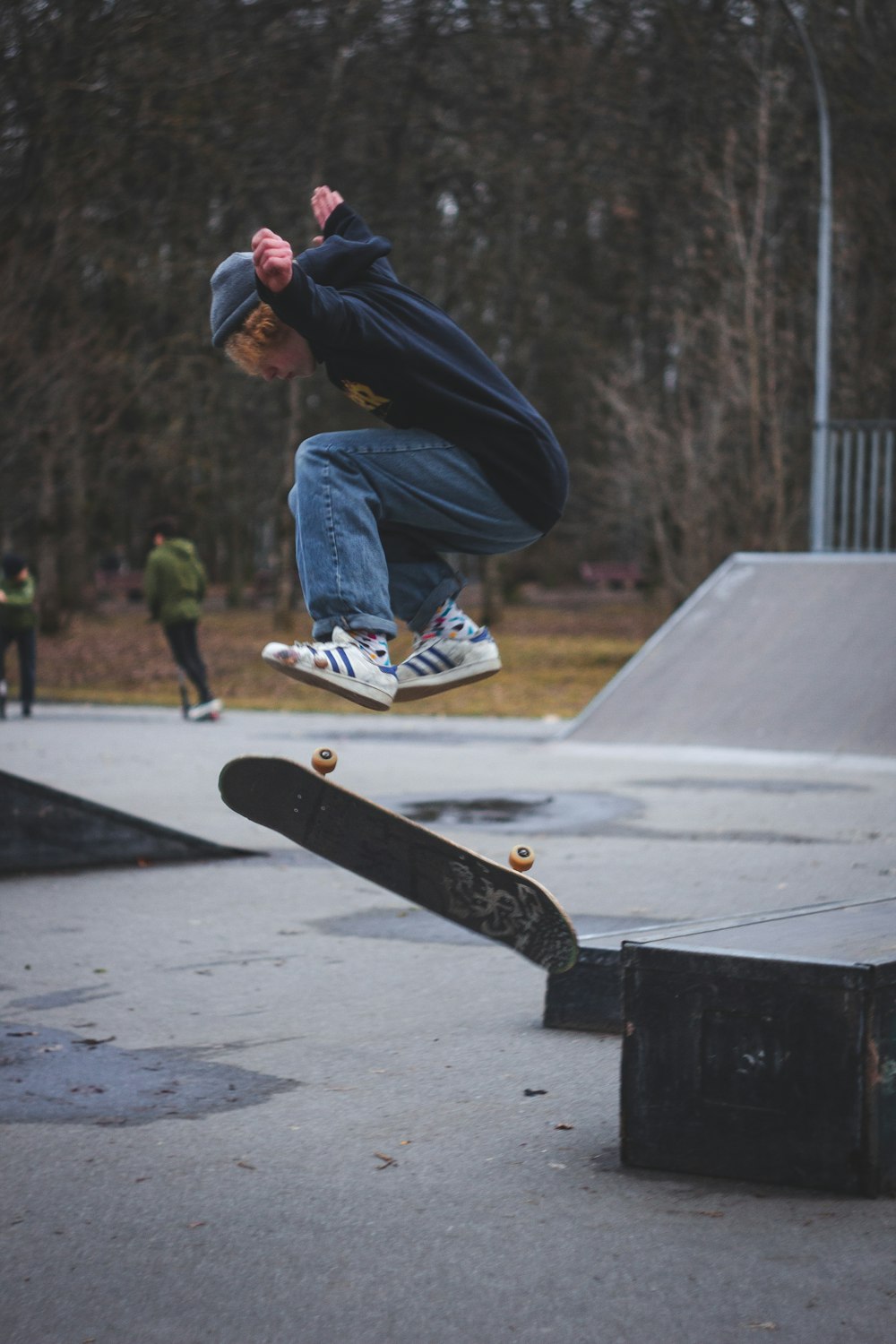 uomo in felpa con cappuccio nera e jeans blu in denim che cavalca lo skateboard durante il giorno