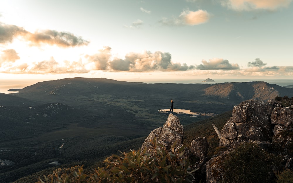 man standing on rock formation under white clouds during daytime