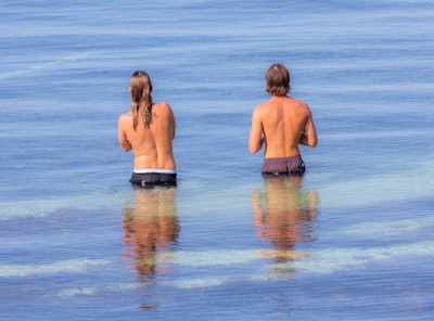 2 women in blue and black shorts standing on water during daytime back google meet background