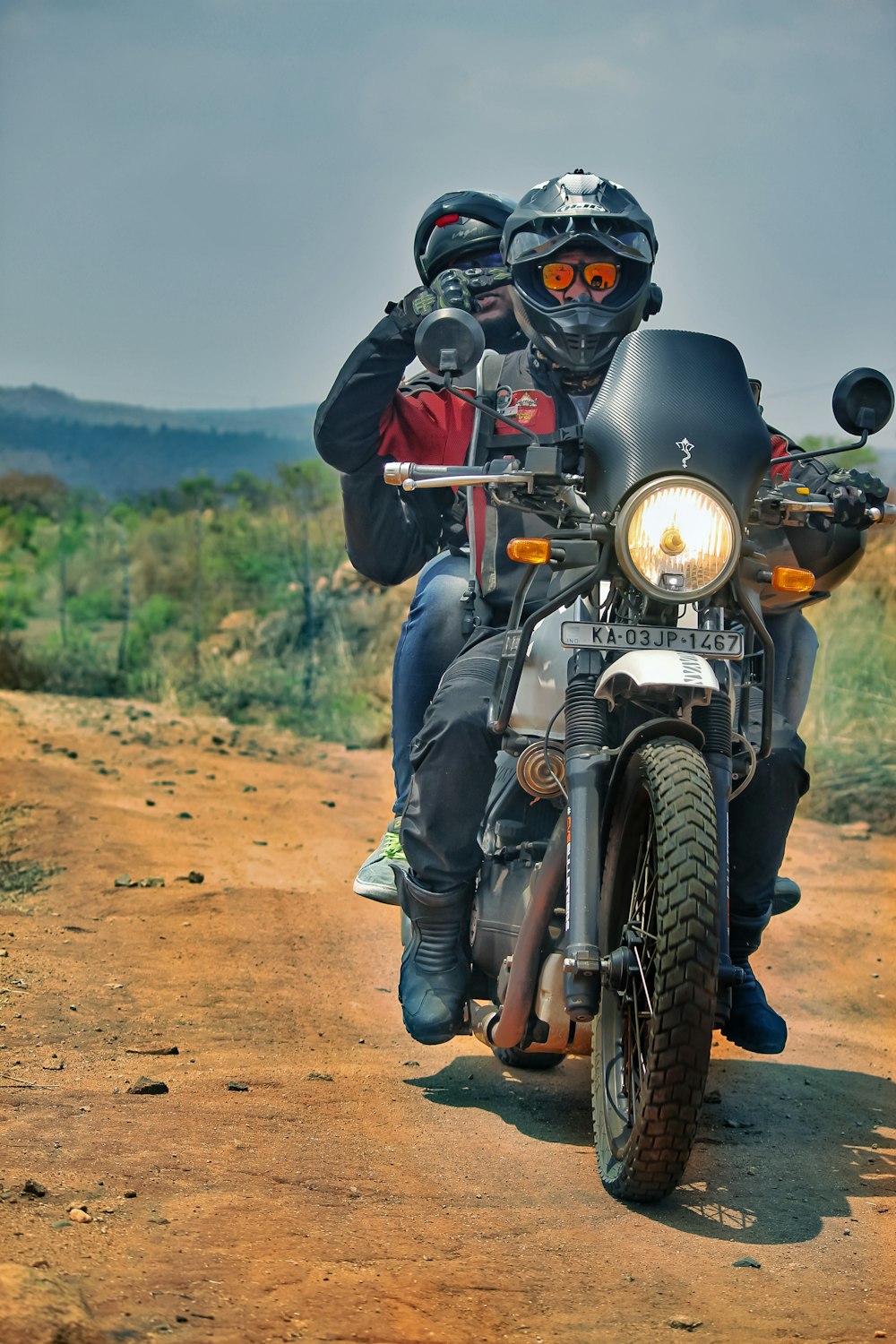 Mann in schwarzer Lederjacke und blauer Jeans fährt schwarzes Motorrad auf braunem Feldweg
