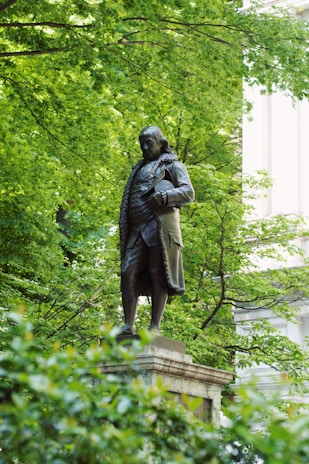 man in coat statue near green trees during daytime
