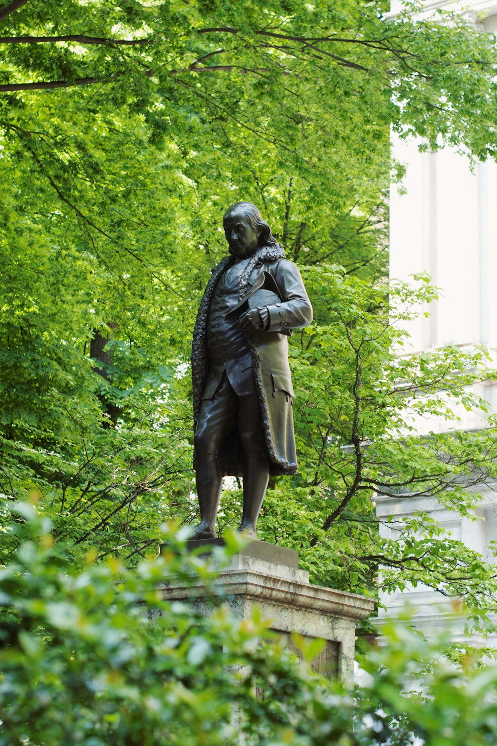 man in coat statue near green trees during daytime