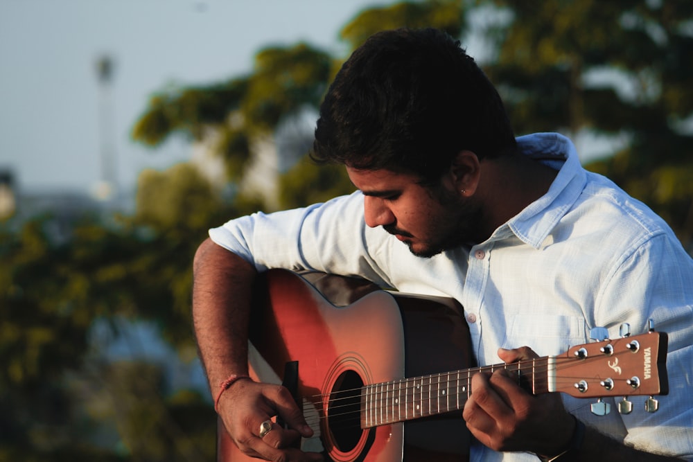 man in white shirt playing acoustic guitar