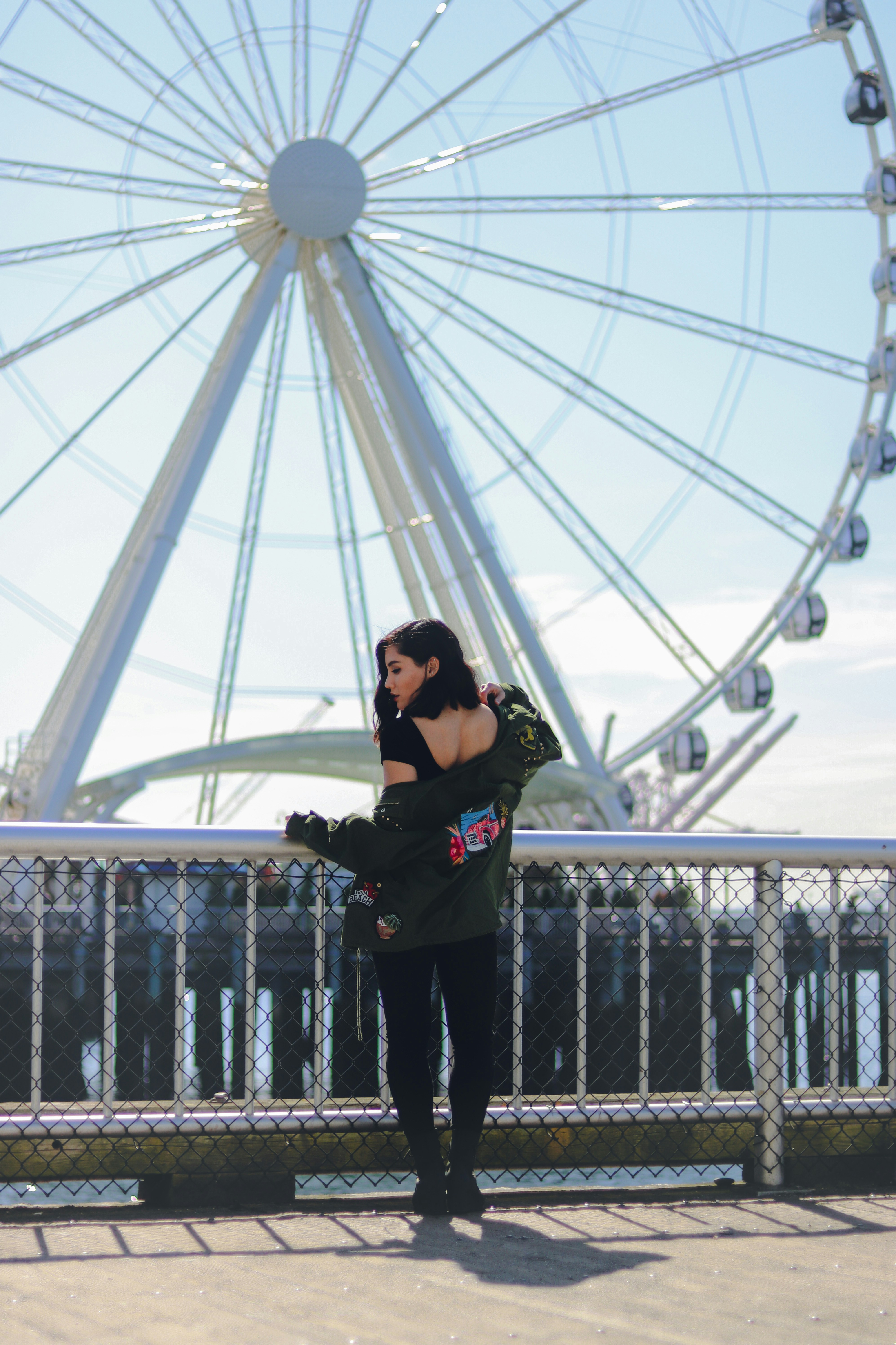 wanita dengan jaket hitam dan celana hitam berdiri di jembatan