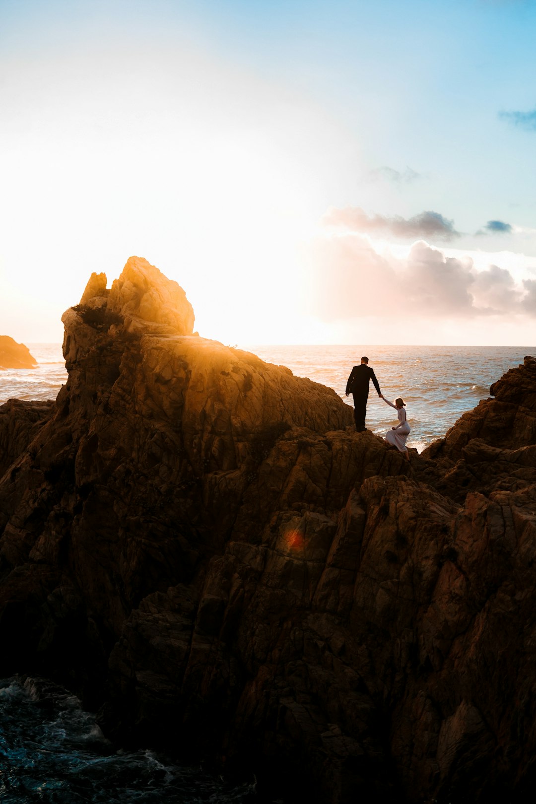 man in black shirt standing on brown rock formation near body of water during daytime