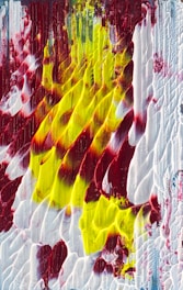 Thick layers of red, yellow, and white paint are applied in a dynamic, textured manner. The colors blend and streak across the canvas, creating a sense of movement and depth.