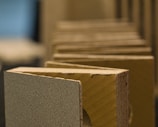 A close-up view of multiple rectangular pieces of a thick material, possibly cardboard or a composite, aligned in a row. The surfaces have a textured appearance, and the edges reveal a layered construction. The background is blurred, emphasizing the focus on the foreground elements.