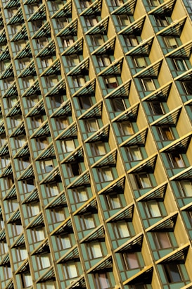 A facade of a building featuring a repeating pattern of triangular protrusions and windows. The structure appears to have a metallic and glass exterior with a geometric design, creating an eye-catching architectural effect.