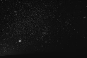 A dark night sky filled with a vast number of stars scattered across the canvas. Several galaxies or nebulae with distinctive circular shapes appear prominently in some areas, providing points of interest among the scattered dots of starlight.