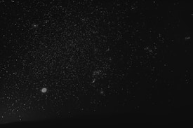 A dark night sky filled with a vast number of stars scattered across the canvas. Several galaxies or nebulae with distinctive circular shapes appear prominently in some areas, providing points of interest among the scattered dots of starlight.