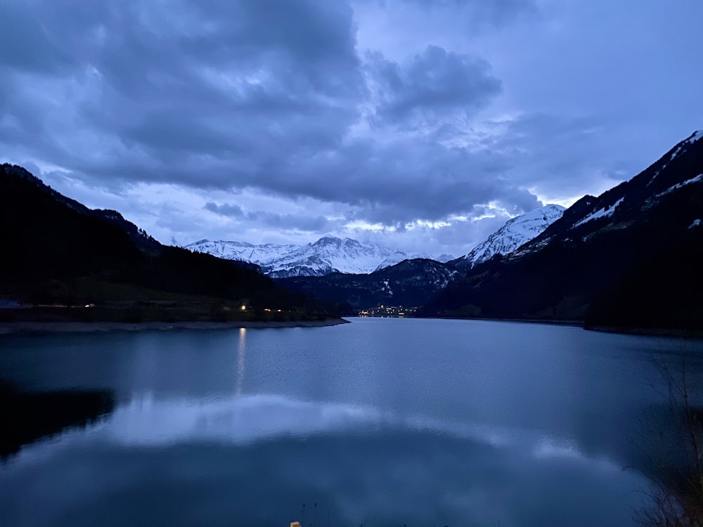 昼間の白い雲の下の山の近くの湖