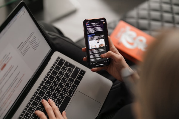 Young caucasian woman on leather couch working at a laptop while browsing her phoneby Maxim Ilyahov