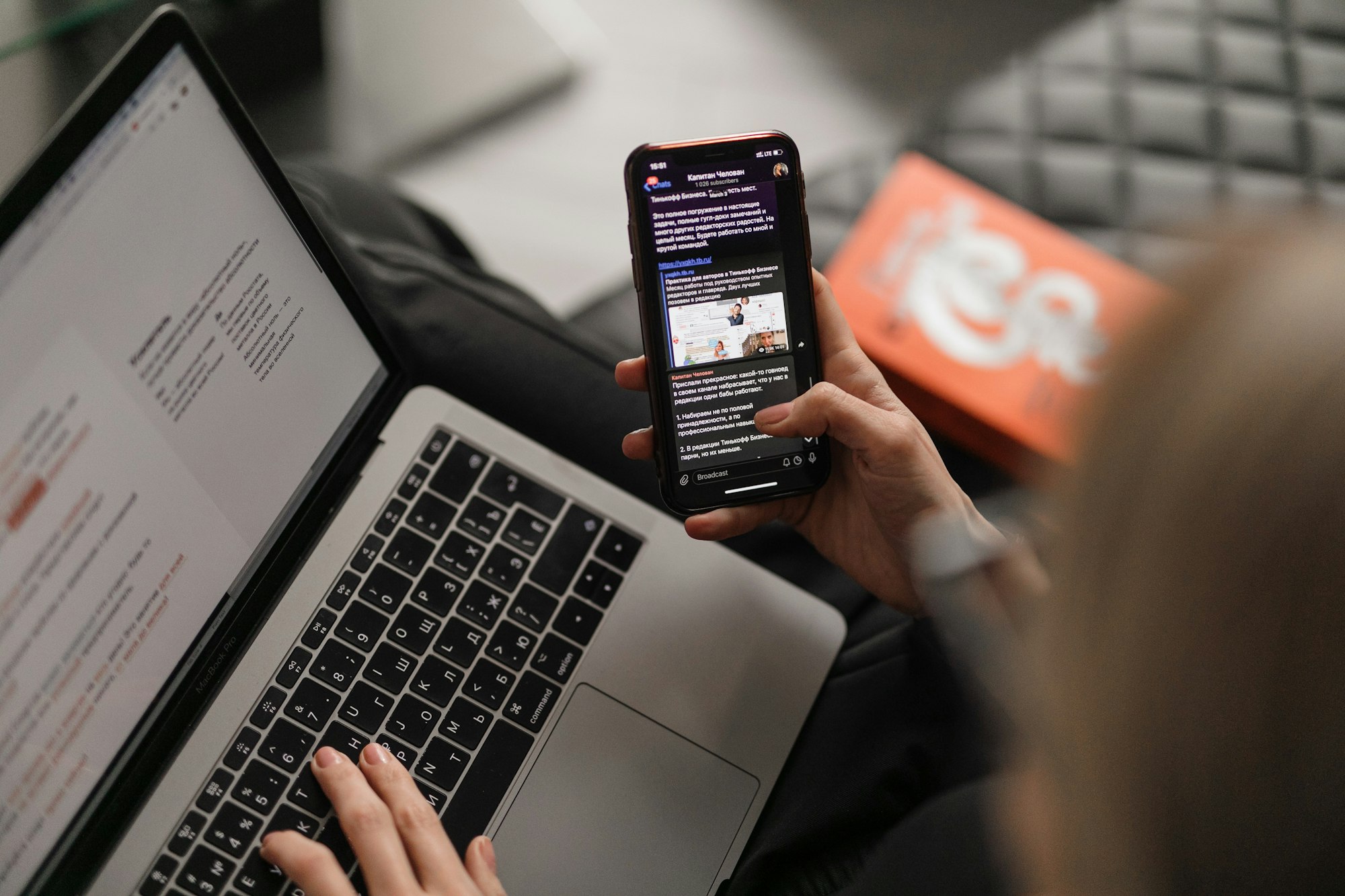 Young caucasian woman on leather couch working at a laptop while browsing her phone