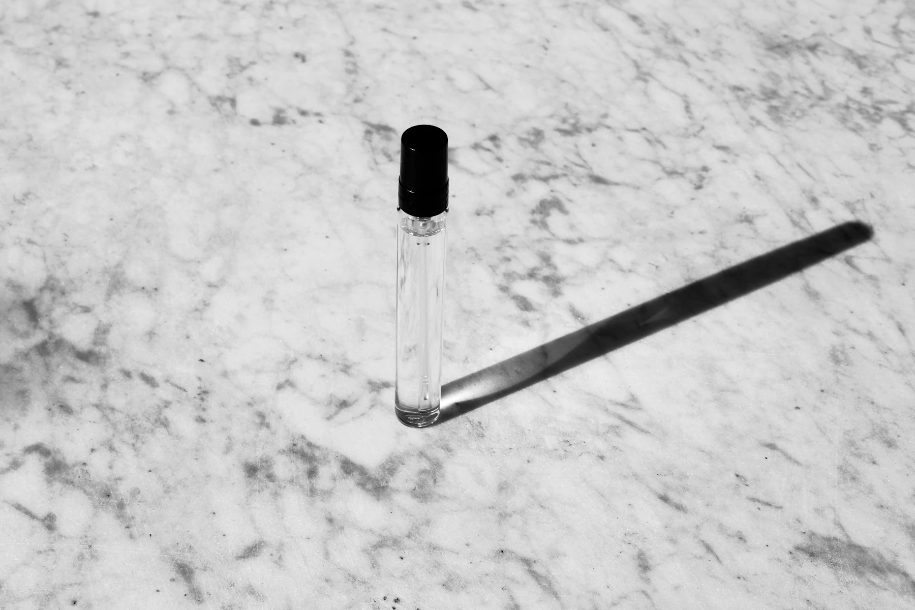 A small glass vial with a black cap casting a long shadow on marble