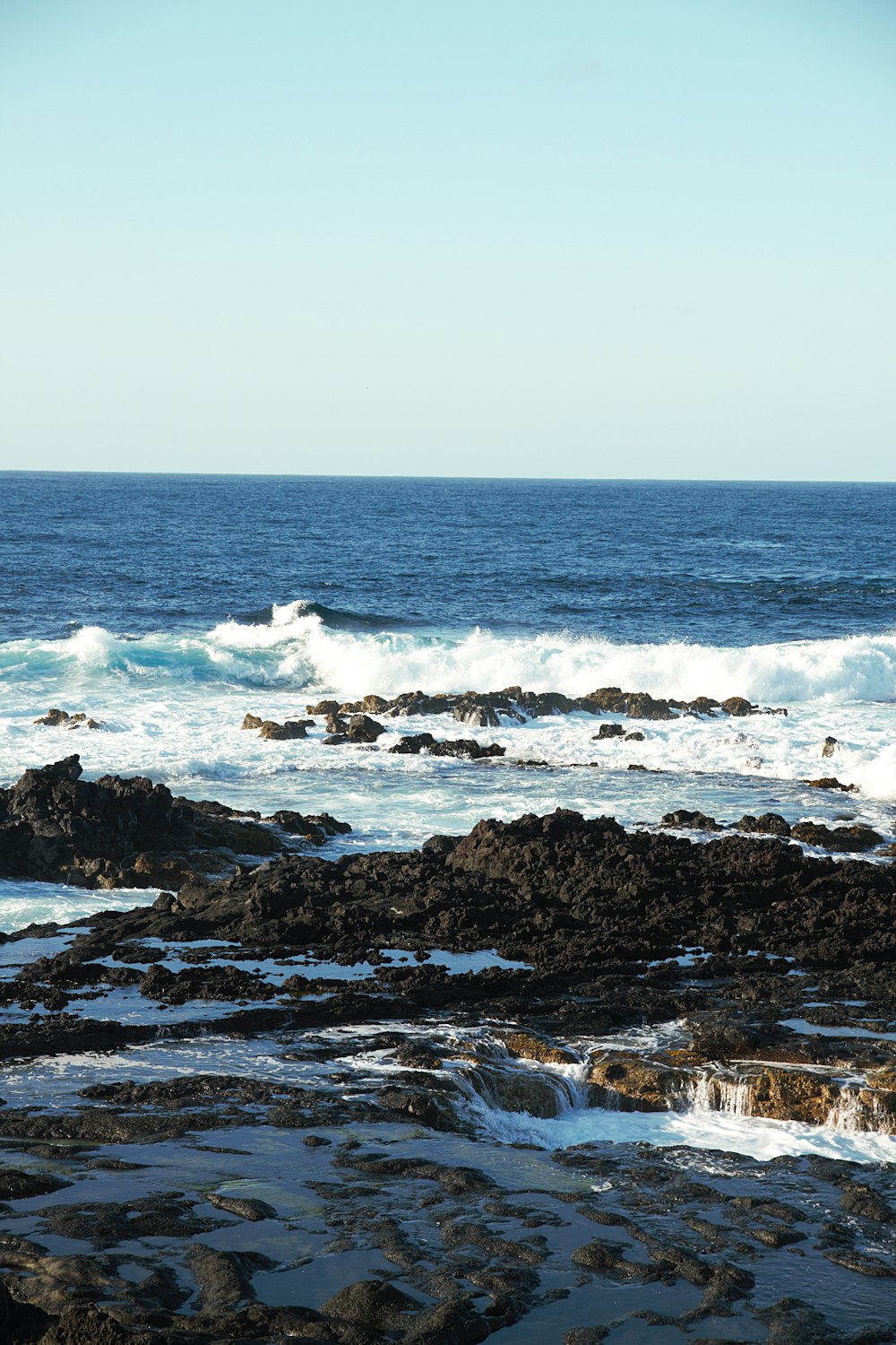 brown rocky shore with ocean waves crashing on shore during daytime