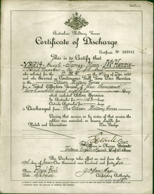 A formal document titled 'Certificate of Discharge' from the Australian Military Forces. It contains printed and handwritten text certifying the discharge of a private, along with dates, service details, and signatures. The background is a light, aged paper, with a green border and an emblem at the top center.