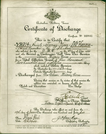 A formal document titled 'Certificate of Discharge' from the Australian Military Forces. It contains printed and handwritten text certifying the discharge of a private, along with dates, service details, and signatures. The background is a light, aged paper, with a green border and an emblem at the top center.