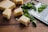 Several cubes of a light yellow cheese are placed on a wooden surface alongside scattered fresh green basil leaves. A metal cheese grater lies nearby.