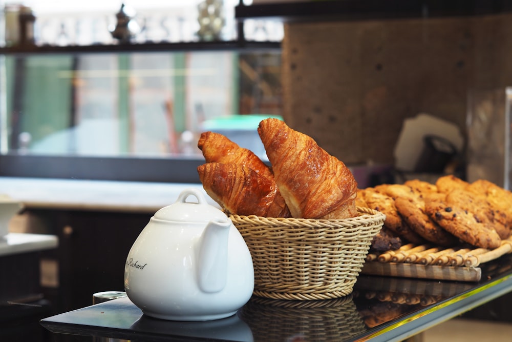 Théière en céramique blanche à côté d’un panier en osier brun sur la table