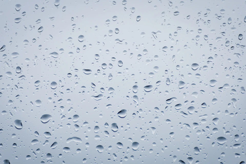 Close-up view of raindrops scattered across a window's surface, reflecting light and contrasting colors
