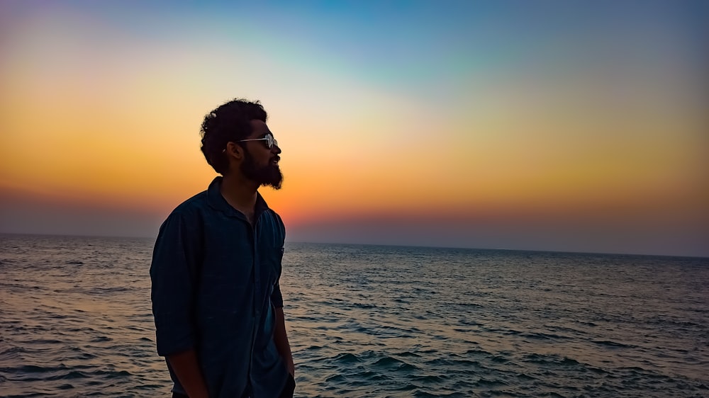 man in blue polo shirt standing on beach during sunset